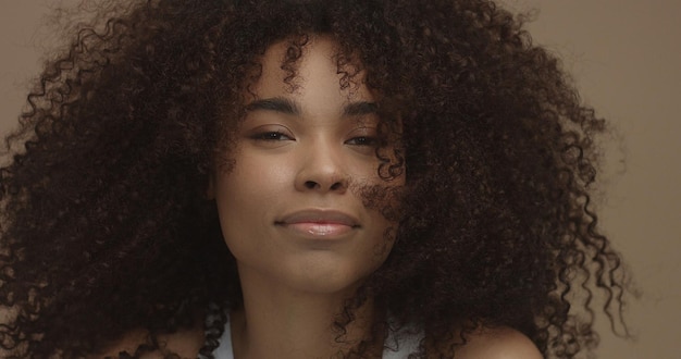 Porträt einer gemischten schwarzen Frau mit großem Afro-Haar, lockigem Haar auf beigem Hintergrund, lächelnd und lachend in der Nähe