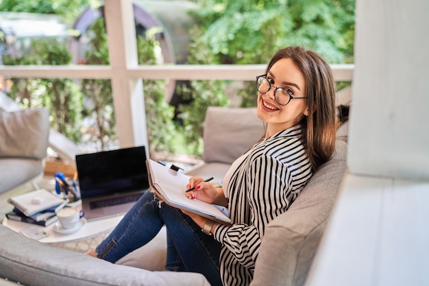 Porträt einer glücklich lächelnden freiberuflichen Frau zu Hause mit Notebook auf dem Sofa.