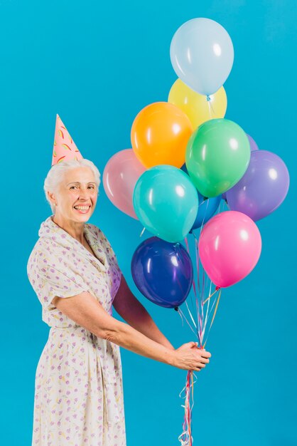 Porträt einer glücklichen älteren Frau mit bunten Ballonen auf blauem Hintergrund