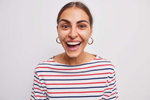 Porträt einer glücklichen brünetten Frau, die gerne auf positive Resonanz reagiert, trägt einen lässigen gestreiften Pullover isoliert über weißer Wand