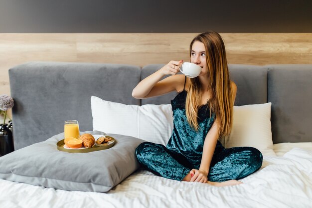 Porträt einer glücklichen Frau, die beim Frühstück im Urlaub im Schlafzimmer denkt und wegschaut