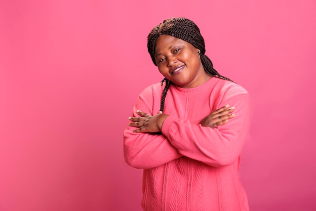 Kostenloses Foto porträt einer glücklichen frau, die selbstbewusst lächelt, während sie im studio posiert, mit fröhlichem gesichtsausdruck und beim fotografieren. afroamerikanisches model mit stylischer frisur und rosafarbenem pullover blickt in die kamera