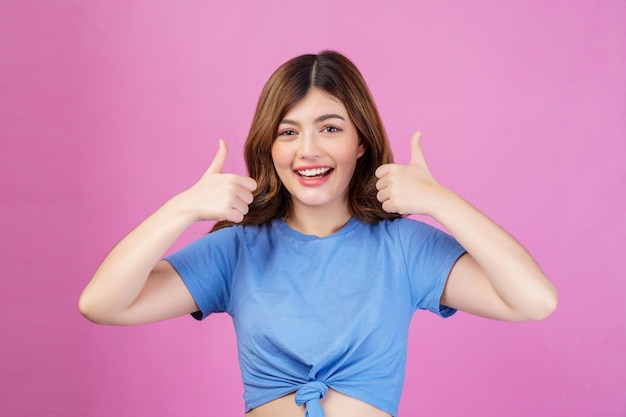 Porträt einer glücklichen jungen Frau, die ein legeres T-Shirt trägt, das den Daumen isoliert über rosa Hintergrund zeigt