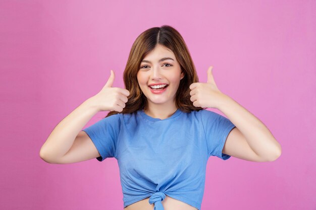 Porträt einer glücklichen jungen Frau, die ein legeres T-Shirt trägt, das den Daumen isoliert über rosa Hintergrund zeigt