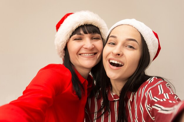Porträt einer glücklichen Mutter und Tochter in der Weihnachtsmütze im Studio auf grauem Hintergrund. Konzept der menschlichen positiven Emotionen und Gesichtsausdrücke