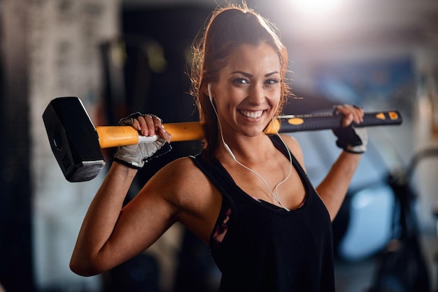 Porträt einer glücklichen Sportlerin mit schwerem Hammer, die beim Cross-Training in einem Fitnessstudio in die Kamera blickt