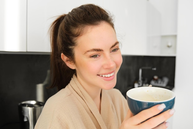 Porträt einer gutaussehenden jungen Frau, die ihren Tag mit einer Tasse Kaffee in der Küche beginnt und