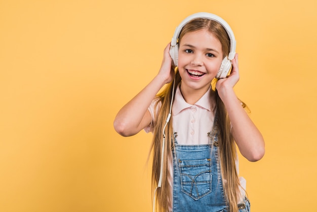 Porträt einer hörenden Musik des glücklichen Mädchens auf Kopfhörer gegen gelben Hintergrund