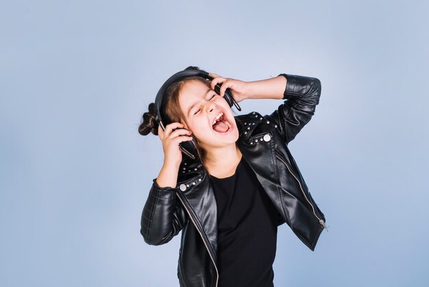 Porträt einer hörenden Musik des Mädchens auf Kopfhörer lachend gegen blauen Hintergrund