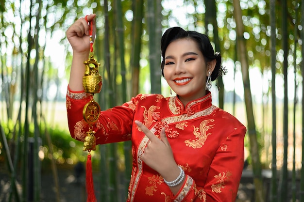 Porträt einer hübschen asiatischen Frau in einem chinesischen Cheongsam-Lächeln und mit goldenem Amulett für glückliche Symboldekorationen des chinesischen Neujahrs