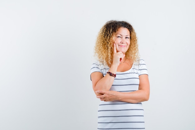 Porträt einer hübschen blonden Frau, die das Kinn in einem gestreiften T-Shirt auf der Hand stützt und eine positive Vorderansicht sieht