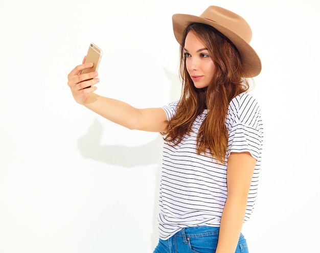 Porträt einer hübschen Frau im Sommerhippie kleidet das Nehmen eines selfie, das auf weißer Wand lokalisiert wird