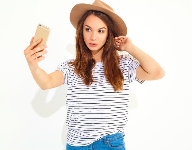 Porträt einer hübschen Frau im Sommerhippie kleidet das Nehmen eines selfie, das auf weißer Wand lokalisiert wird