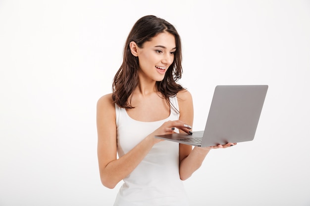 Porträt einer hübschen Frau kleidete im Trägershirt unter Verwendung des Laptops an