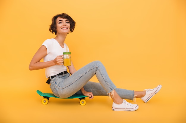 Porträt einer hübschen niedlichen Frau, die auf einem Skateboard sitzt