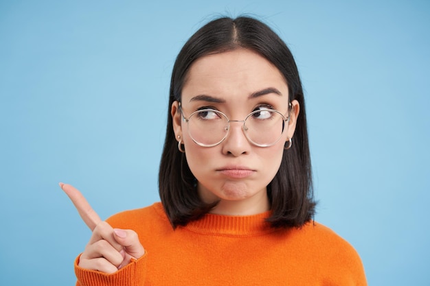 Kostenloses Foto porträt einer japanischen frau mit brille, die nach links zeigt und zur seite blickt, während banner über dem blauen studiorücken stehen