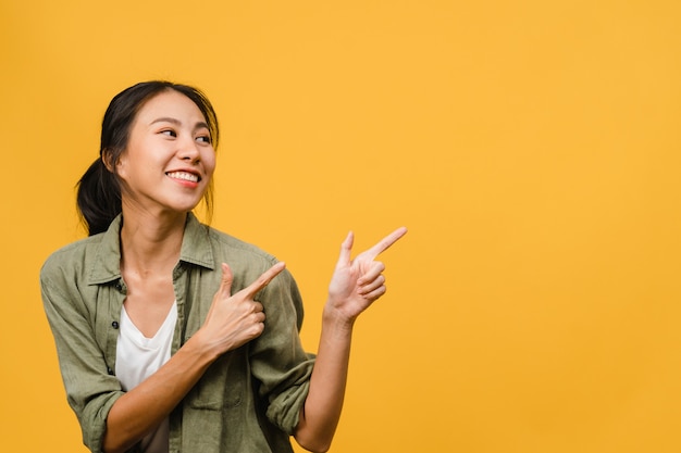 Porträt einer jungen asiatischen Dame, die mit fröhlichem Ausdruck lächelt, zeigt etwas Erstaunliches an leeren Stellen in Freizeitkleidung und steht isoliert über gelber Wand. Gesichtsausdruck Konzept.