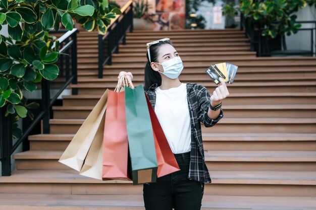 Porträt einer jungen asiatischen Frau in Schutzmaske, Brille auf dem Kopf stehend mit Einkaufspapiertüte