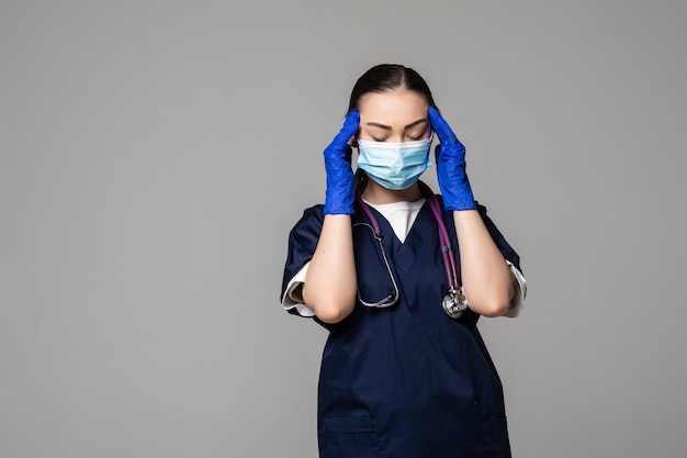 Porträt einer jungen asiatischen Ärztin, die medizinische Gesichtsmaske, Handschuhe und Stethoskop trägt, nach oben schaut und nachdenkt, isoliert auf grauer Wand