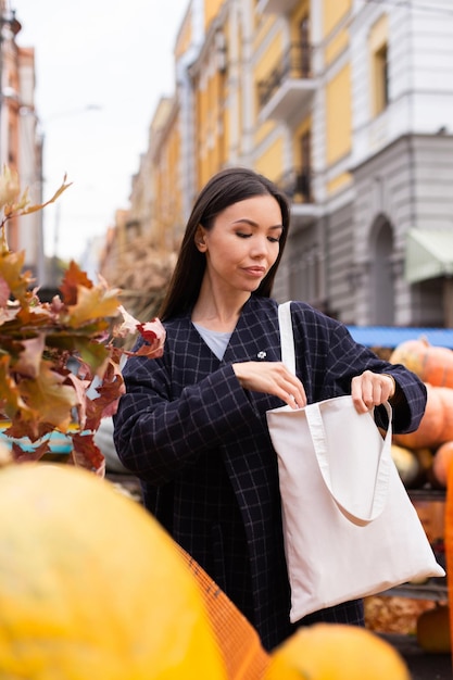 Porträt einer jungen, attraktiven, lässigen Frau, die im Herbst-Hofladen im Freien nach Geldbeutel in der Tasche sucht