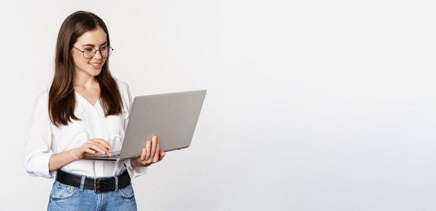 Porträt einer jungen Bürofrau, die Kunden auf einem Laptop beantwortet, der mit einem Computer mit Happ arbeitet