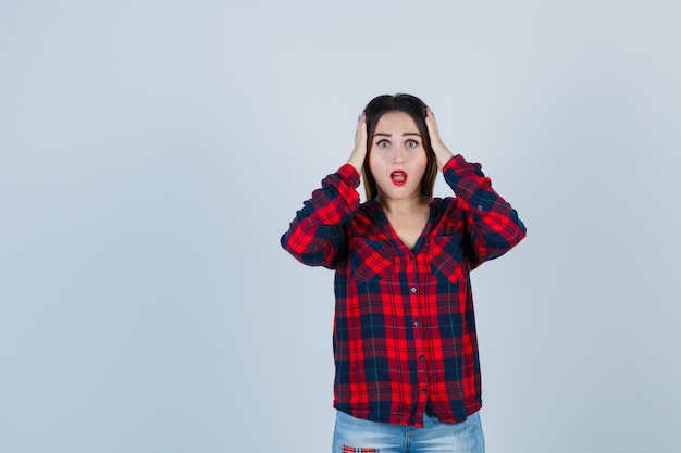 Porträt einer jungen Dame mit den Händen auf dem Kopf in kariertem Hemd, Jeans und versteinerter Vorderansicht