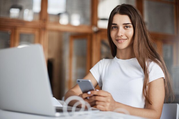 Porträt einer jungen Dame mit Laptop und Handy in der Universitätsbibliothek, die sich auf ihre Abschlussprüfungen vorbereitet Junge Berufstätige, die ihren Karriereweg beginnen Bildungskonzept