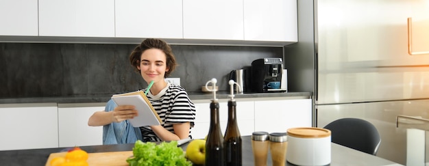 Porträt einer jungen Frau, die auf der Küchenplatte Zutaten kocht und Notizen schreibt