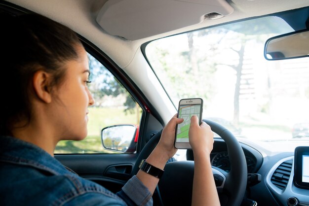 Porträt einer jungen Frau, die das GPS-Navigationssystem auf ihrem Mobiltelefon verwendet, während sie ihr Auto fährt