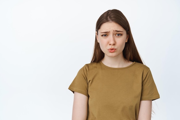 Porträt einer jungen Frau, die die Stirn runzelt, mit Unbehagen autsch sagt, Mitleid mit jemandem hat, etw verletzend oder schlecht beobachtet, krampfhafter Ausdruck, weißer Hintergrund