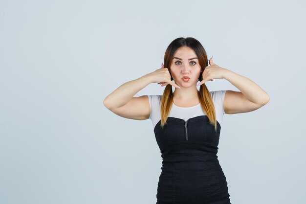 Porträt einer jungen Frau, die eine Telefongeste zeigt, während sie die Lippen schmollend