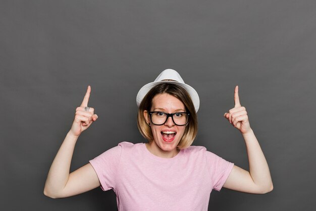 Porträt einer jungen Frau, die Finger gegen graue Wand aufwärts zeigend lacht