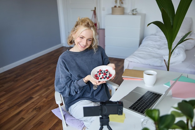 Porträt einer jungen Frau, die mit dem Publikum spricht und einen Vlog mit digitaler Kamera aufnimmt, der ihr Frühstück zeigt