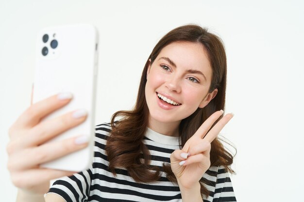 Porträt einer jungen Frau, die mit einem Smartphone Selfies macht und mit einer Handy-App für Fotos posiert