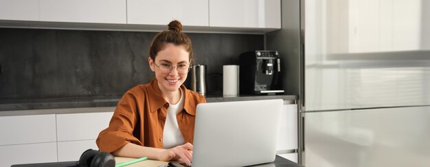 Kostenloses Foto porträt einer jungen frau, die von zu hause aus arbeitet und einen arbeitsplatz in der küche mit einem laptop einrichtet