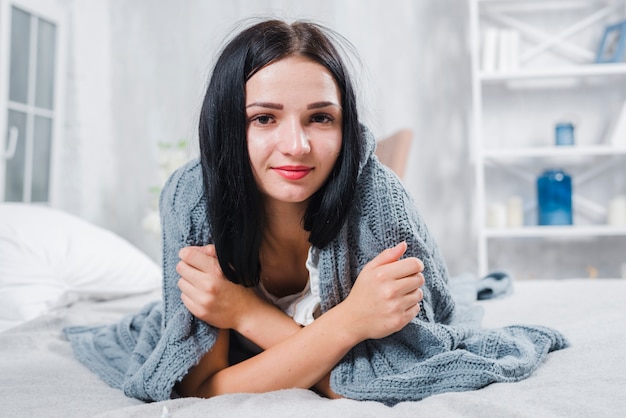 Porträt einer jungen Frau eingewickelt im Schal, der das Fieber hat, das auf Bett liegt