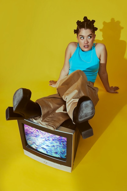 Porträt einer jungen Frau im Modestil der 2000er Jahre, die zusammen mit einem Fernseher posiert