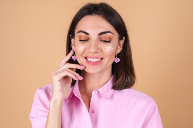 Porträt einer jungen Frau in einem rosa Kleid mit glänzendem Glitzer-Make-up und süßen Ohrringen, die positiv posieren