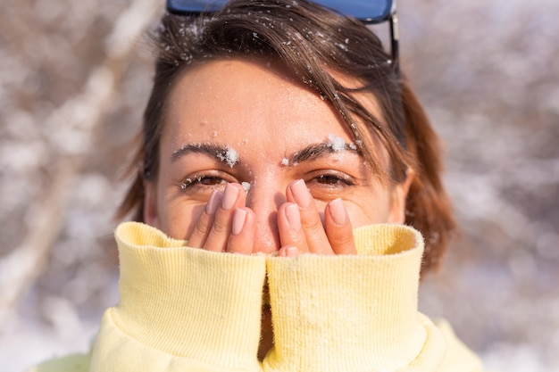 Porträt einer jungen Frau in einem Winterwald an einem sonnigen Tag mit einem schneeweißen Lächeln, das herumalbert