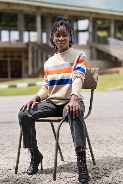 Kostenloses Foto porträt einer jungen frau mit afro-dreadlocks, die draußen auf einem stuhl sitzt