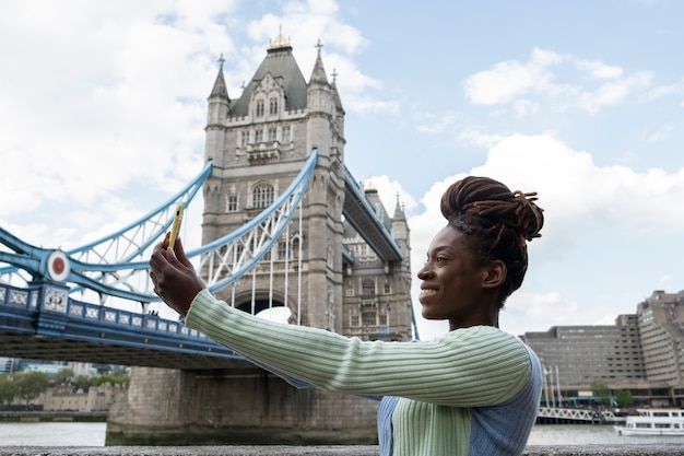 Porträt einer jungen Frau mit Afro-Dreadlocks, die neben einer Brücke in der Stadt ein Selfie macht