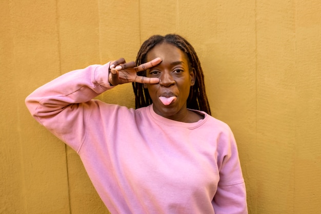 Kostenloses Foto porträt einer jungen frau mit afro-dreadlocks, die posiert und ein friedenszeichen zeigt