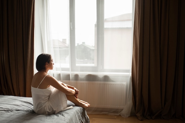 Porträt einer jungen Frau mit geringem Selbstwertgefühl, die zu Hause im Bett sitzt