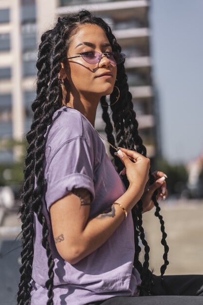 Porträt einer jungen Frau mit langen Haaren, die ein lila Hemd und eine Sonnenbrille trägt