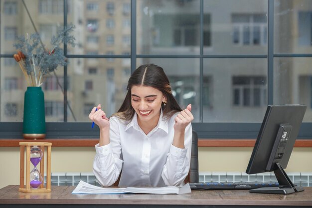 Porträt einer jungen Geschäftsfrau, die am Schreibtisch sitzt und ihre Fäuste zusammendrückt Foto in hoher Qualität
