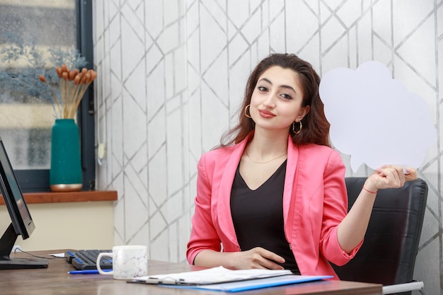 Porträt einer jungen Geschäftsfrau, die hinter dem Schreibtisch sitzt und in die Kamera schaut