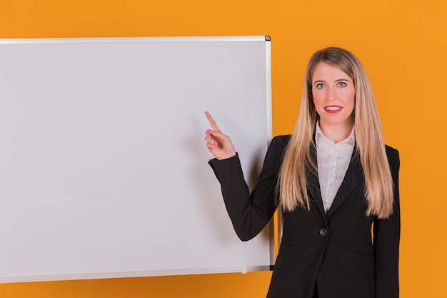 Kostenloses Foto porträt einer jungen geschäftsfrau, die ihren finger auf whiteboard gegen einen orange hintergrund zeigt