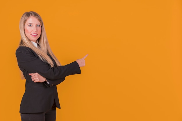 Porträt einer jungen Geschäftsfrau, die ihren Finger gegen einen orange Hintergrund zeigt