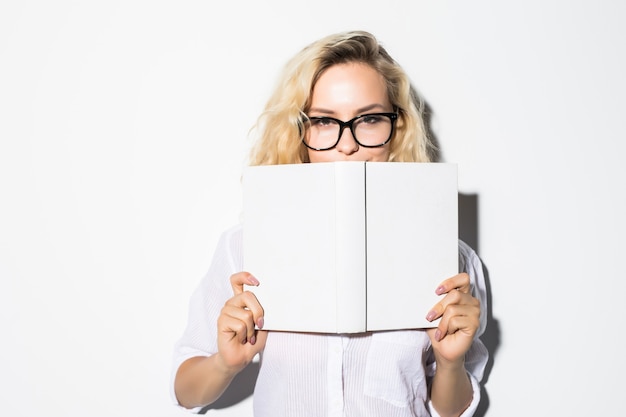 Porträt einer jungen Geschäftsfrau, die sich hinter einem Buch mit Brille versteckt, lokalisiert auf einer grauen Wand
