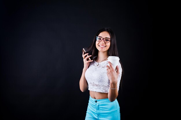 Porträt einer jungen glücklichen Frau in weißem Oberteil und blauer Hose mit einer Tasse Kaffee in der Hand